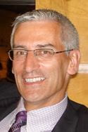 Close up image of a man, wearing glasses and a suit. 