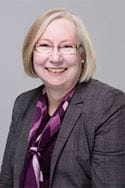 Portrait image of woman with blonde hair and glasses, wearing a suit. 