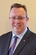 Portrait style image of a man with glasses, wearing a suit.