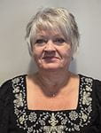 Terry Bauer - photo of a woman with short, grey hair and a black, beaded top.