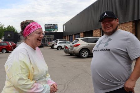 A man and a woman laughing while standing in a parking lot.