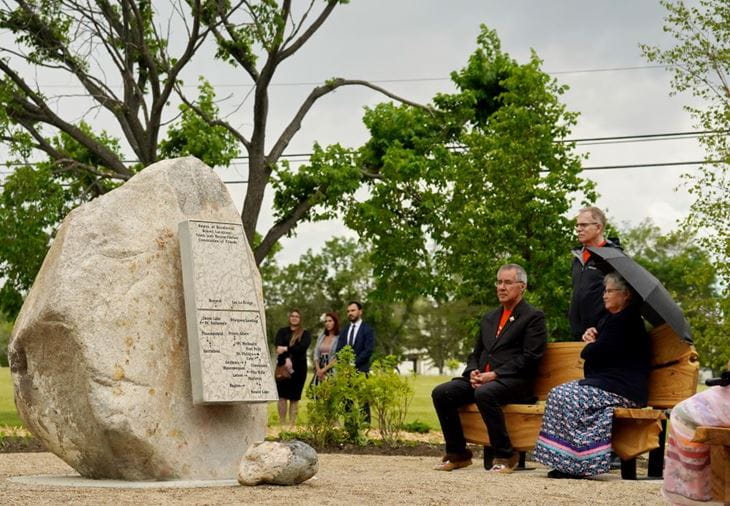 Russ Donna Mirasty seated in rain near centre stone at Memorial Dedication on June 21, 2022.