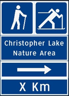 Blue sign with stick men hiking and cross country skiing with directions to Christopher Lake Nature Area