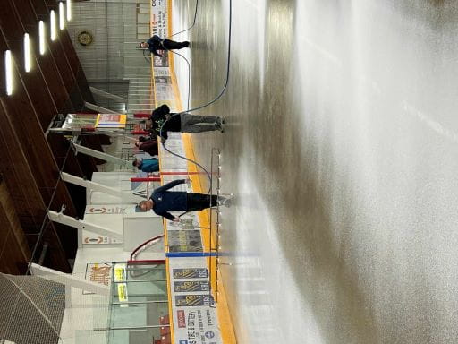 Three people painting the ice on an indoor skating rink.