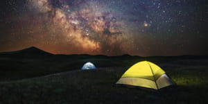 Grasslands National Park. A nighttime scene featuring two tents illuminated by flashlights. The sky overhead is full of stars.