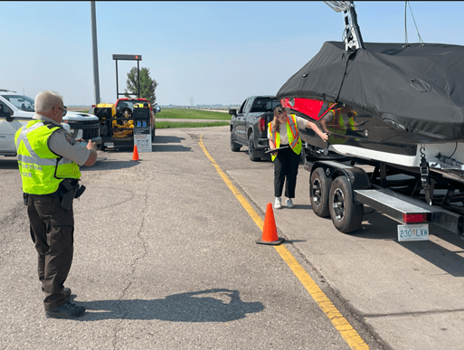Picture of watercraft inspection station in Saskatchewan, a vehicle towing a boat pulled over and being inspected by a conversation officer in uniform