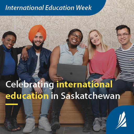 Five students sit on a bench together, smiling at the camera, while the student in the middle has a laptop resting on her lap. 