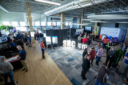 Attendees at the Saskatchewan Research Council’s Tech Expo event are seen speaking with hosts of various display booths set up in a large conference room.