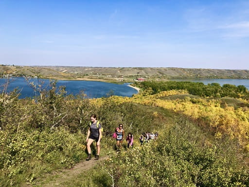 A Park Interpreter in shorts and t-shirt hikes on a sunny fall day with a group of people behind her.