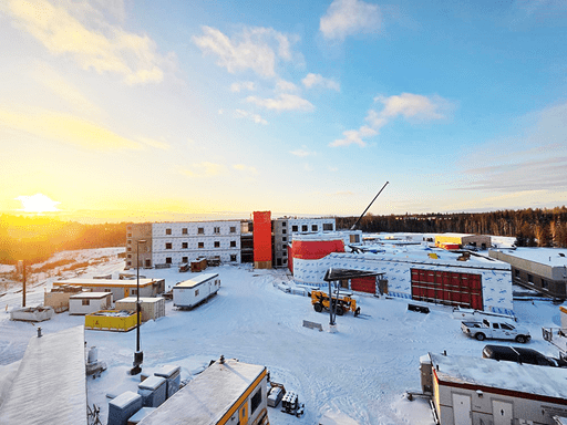 Aerial view of La Ronge Long-Term Care Home at 50% construction with snow on the ground and sunrise or senset backdrop.